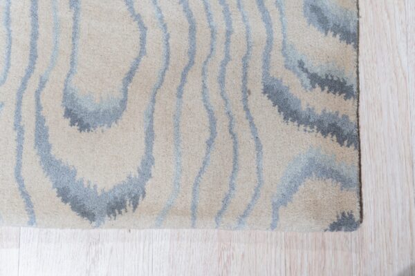 High-pile rug with abstract beige, blue, and gray wavy stripes on light plank flooring.