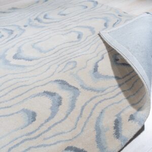 Cream and gray abstract rug rolled back on light wood flooring, showing the fabric backing.