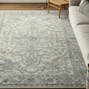 Cream and grey traditional area rug on wood flooring next to a light sofa and rattan chair.