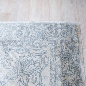 Textured off-white rug with a light blue traditional pattern resting on pale wood flooring.