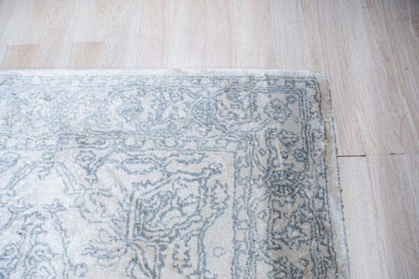 Textured off-white rug with a light blue traditional pattern resting on pale wood flooring.