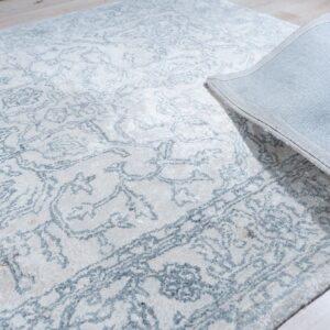 Cream rug with a faded blue ornate pattern lies on light wood flooring, revealing a gray fabric backing.
