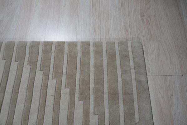 A textured beige rug with staggered vertical stripes sits on light wood flooring.