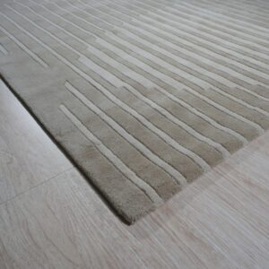 Textured beige rug with alternating carved stripes lying on light-colored wood plank flooring.