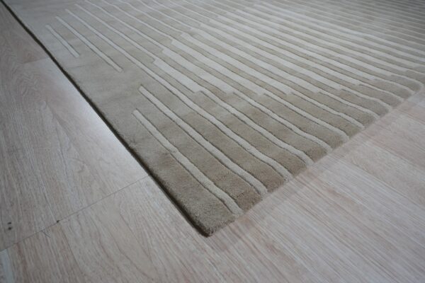 Textured beige rug with alternating carved stripes lying on light-colored wood plank flooring.