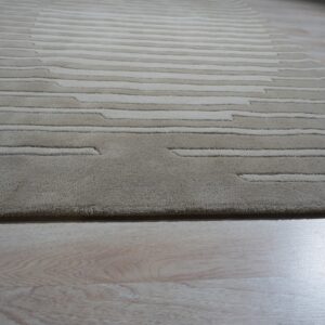 A beige textured rug with carved horizontal stripes lies on glossy light wood flooring.