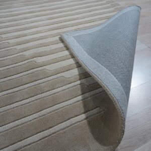 Beige striated rug partially lifted, showing a woven gray backing against pale wood flooring.