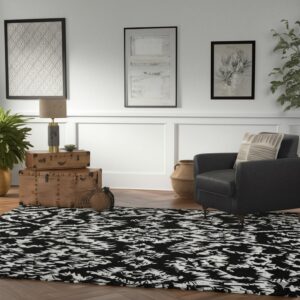 Abstract black and white rug on herringbone wood flooring next to a dark leather armchair.
