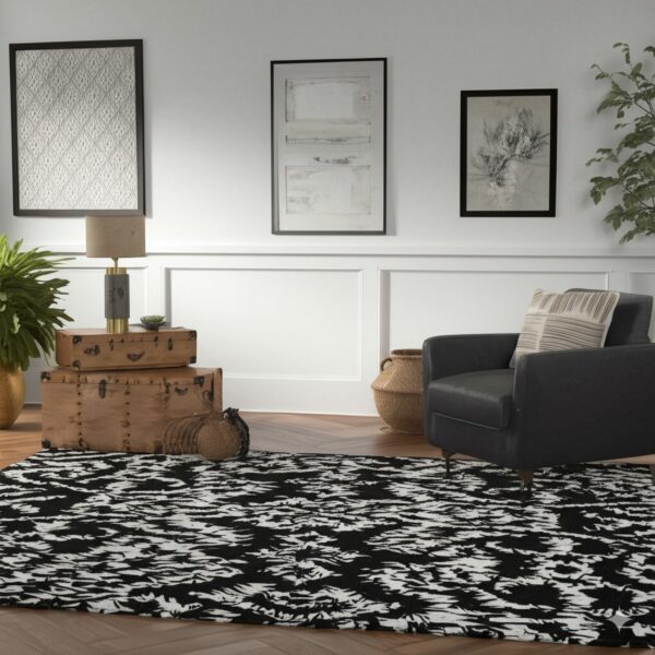 Abstract black and white rug on herringbone wood flooring next to a dark leather armchair.