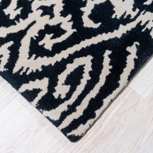 A black and beige abstract pattern rug corner rests on light wood plank flooring.