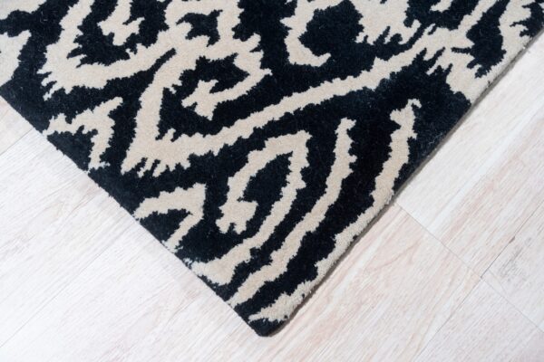 A black and beige abstract pattern rug corner rests on light wood plank flooring.
