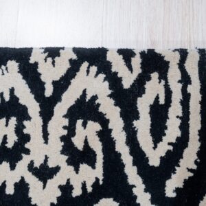 A black and cream abstract high-pile rug with organic patterns rests on pale wood flooring.
