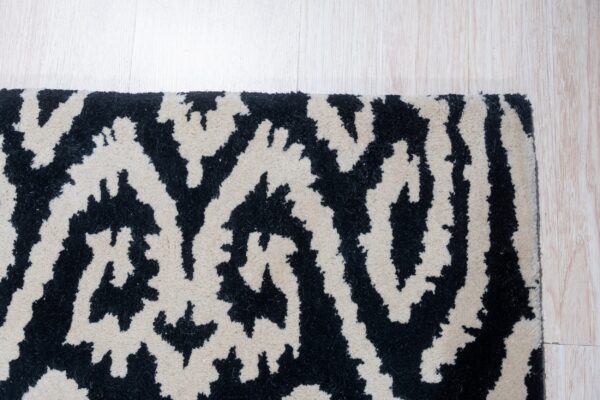 A black and cream abstract high-pile rug with organic patterns rests on pale wood flooring.