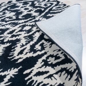 Abstract black and cream rug partially folded, showing fabric backing on light wood floor.