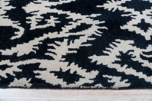 Close-up of a black and cream abstract patterned rug showing a textured pile resting on light wood flooring.