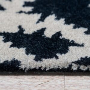 Detailed view of a thick, fluffy black and cream abstract rug pile edge resting on light wood flooring.