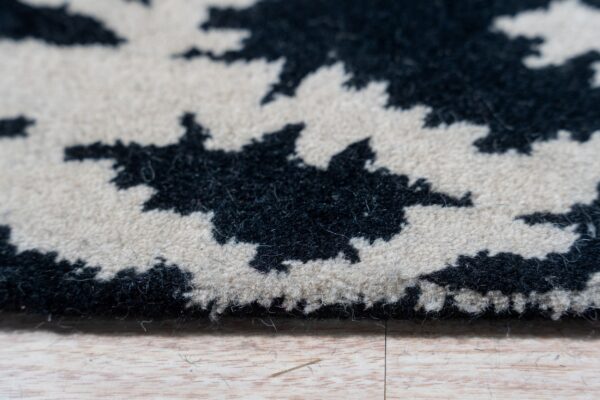 Detailed view of a thick, fluffy black and cream abstract rug pile edge resting on light wood flooring.