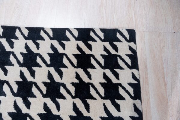 Black and beige rug with a houndstooth design sits on pale wooden plank flooring.