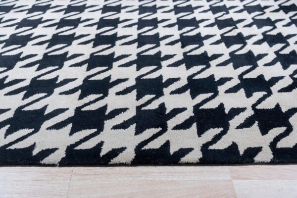 Black and cream high-pile rug with a houndstooth pattern rests on light wood plank flooring.