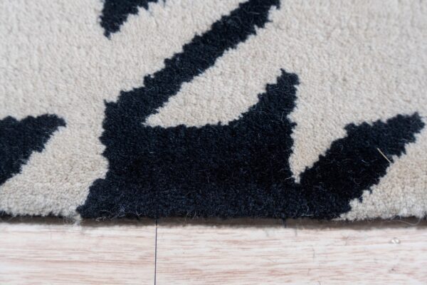 Dense black and cream high-pile rug with an irregular pattern rests on light wooden plank flooring.