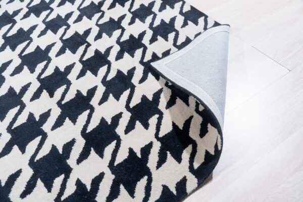 Black and cream houndstooth patterned rug with a corner folded back on light wood floor.