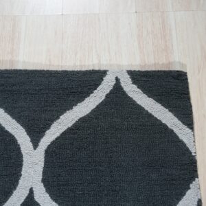 A dark grey textural rug with a thick light grey trellis pattern rests on pale wooden flooring.