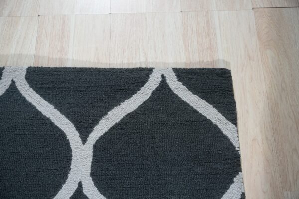 A dark grey textural rug with a thick light grey trellis pattern rests on pale wooden flooring.