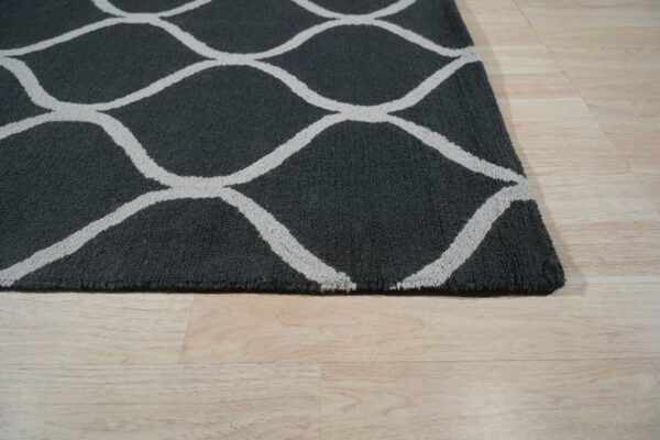 Charcoal gray rug with a light gray wavy geometric pattern rests on light wood planks.