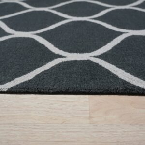 Medium pile charcoal rug with an off-white geometric trellis pattern on pale wood flooring.
