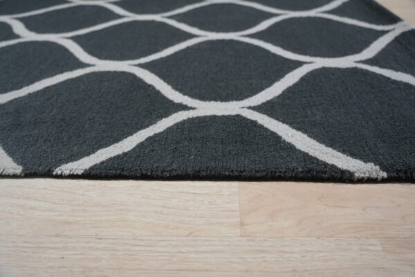 Medium pile charcoal rug with an off-white geometric trellis pattern on pale wood flooring.