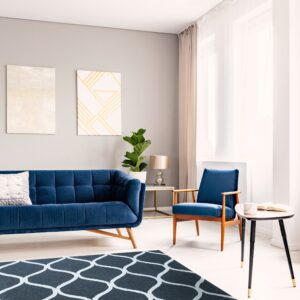 Charcoal and white ogee patterned rug on a light floor beneath a blue sofa and armchair.