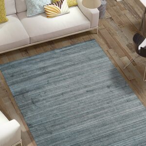 Large slate blue area rug with horizontal striations rests on wood flooring beside a white couch.