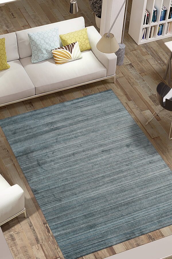 Large slate blue area rug with horizontal striations rests on wood flooring beside a white couch.