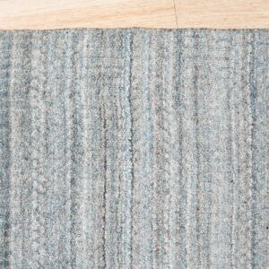 The edge of a textured gray and light blue striped rug lies on pale blonde flooring.