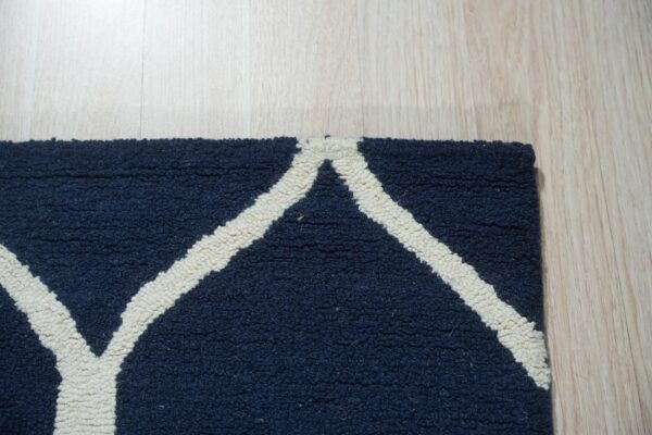 Textured navy blue rug with cream geometric lines lying on light wood flooring.