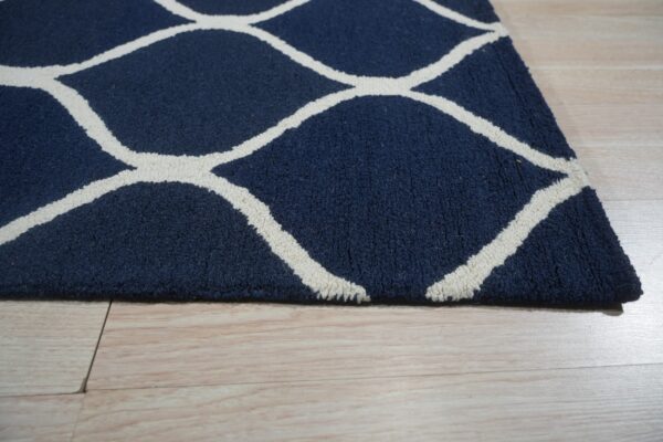 Navy blue rug with a textured white geometric pattern rests on light blonde flooring.
