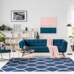 A navy blue rug with a repeating white ogee pattern anchors a living room with teal velvet furniture.