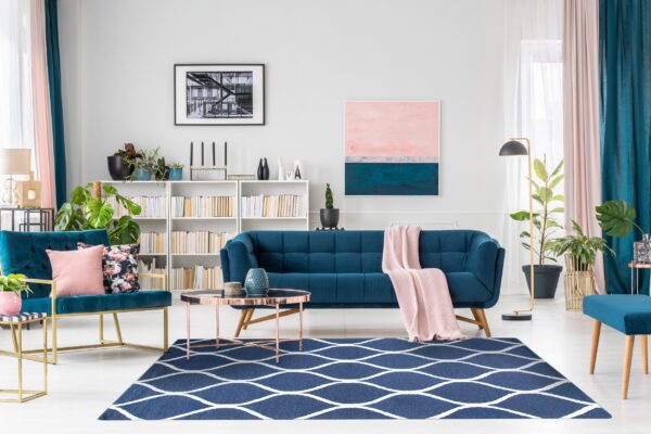 A navy blue rug with a repeating white ogee pattern anchors a living room with teal velvet furniture.