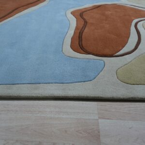 High-pile abstract rug with carved shapes in light blue, rust, beige, and yellow resting on wood floor.