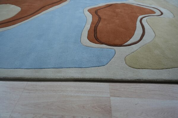 High-pile abstract rug with carved shapes in light blue, rust, beige, and yellow resting on wood floor.