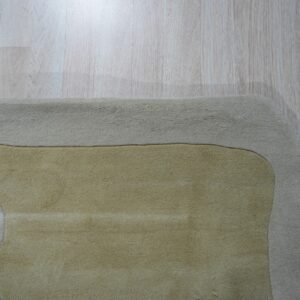 A soft pile rug displays abstract curves in beige, gold, and brown tones on light wood plank flooring.