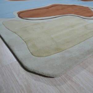 Sculpted rug with blue, rust, and beige organic shapes resting on light wood planks.