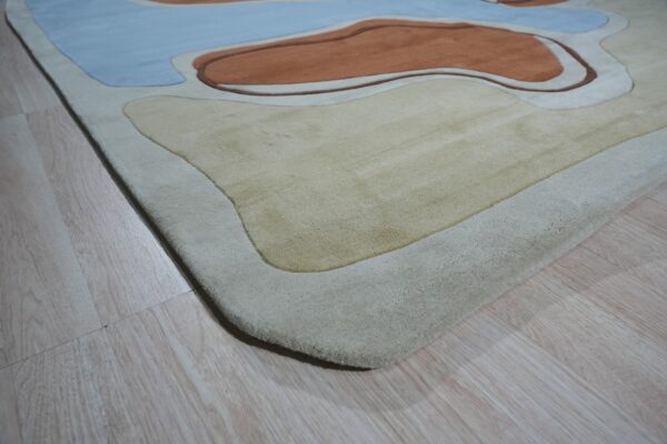 Sculpted rug with blue, rust, and beige organic shapes resting on light wood planks.
