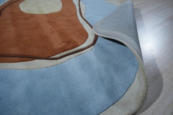Abstract brown and blue high-pile rug partially rolled back to show the gray fabric backing on light wood flooring.
