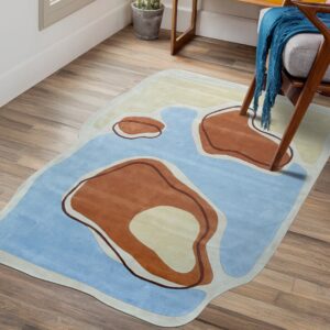 Irregularly shaped rug in blue, terracotta, and cream sits on wood planks next to an armchair.