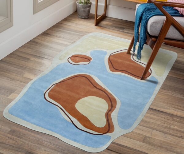 Irregularly shaped rug in blue, terracotta, and cream sits on wood planks next to an armchair.