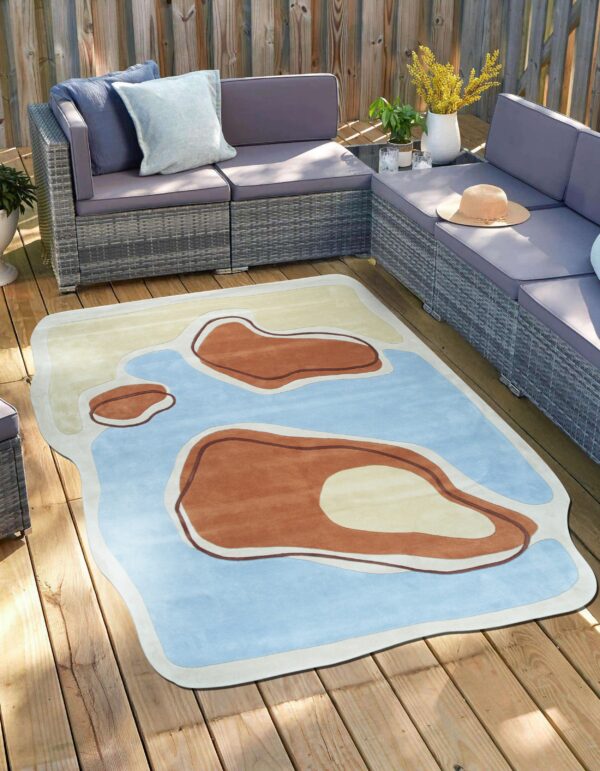 An irregularly shaped rug with blue, tan, and brown organic forms is on a sunny wooden outdoor deck.