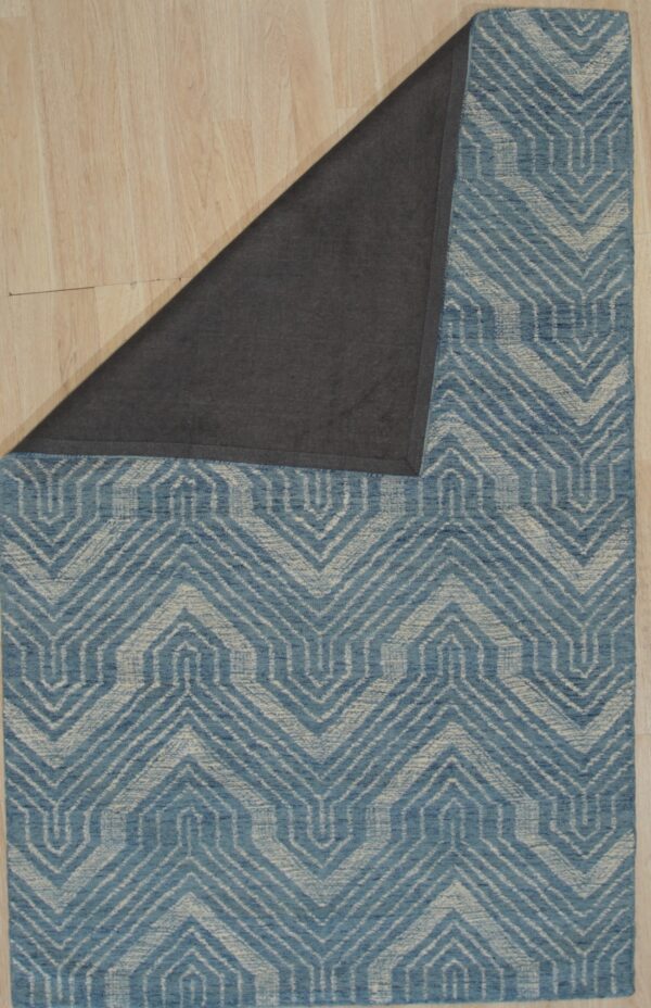 Blue and beige geometric rug on light wood floor, folded back to reveal the dark gray backing material.