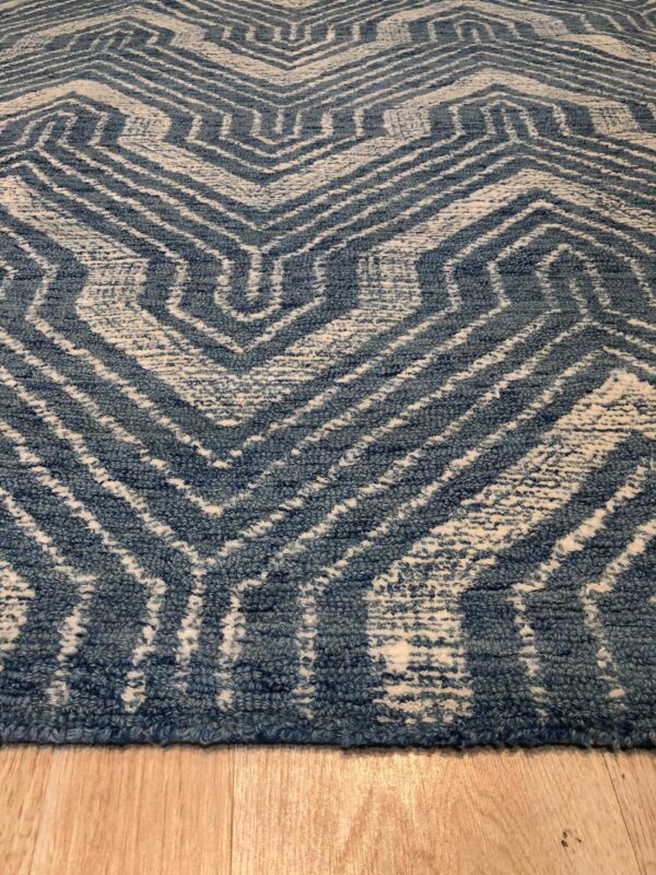 Distressed blue and cream high-pile rug featuring a geometric interlocking zigzag pattern on wood flooring.