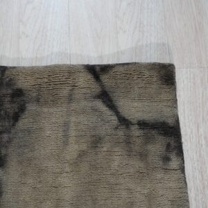 A textured brown and black abstract rug edge rests on light blonde wood flooring.